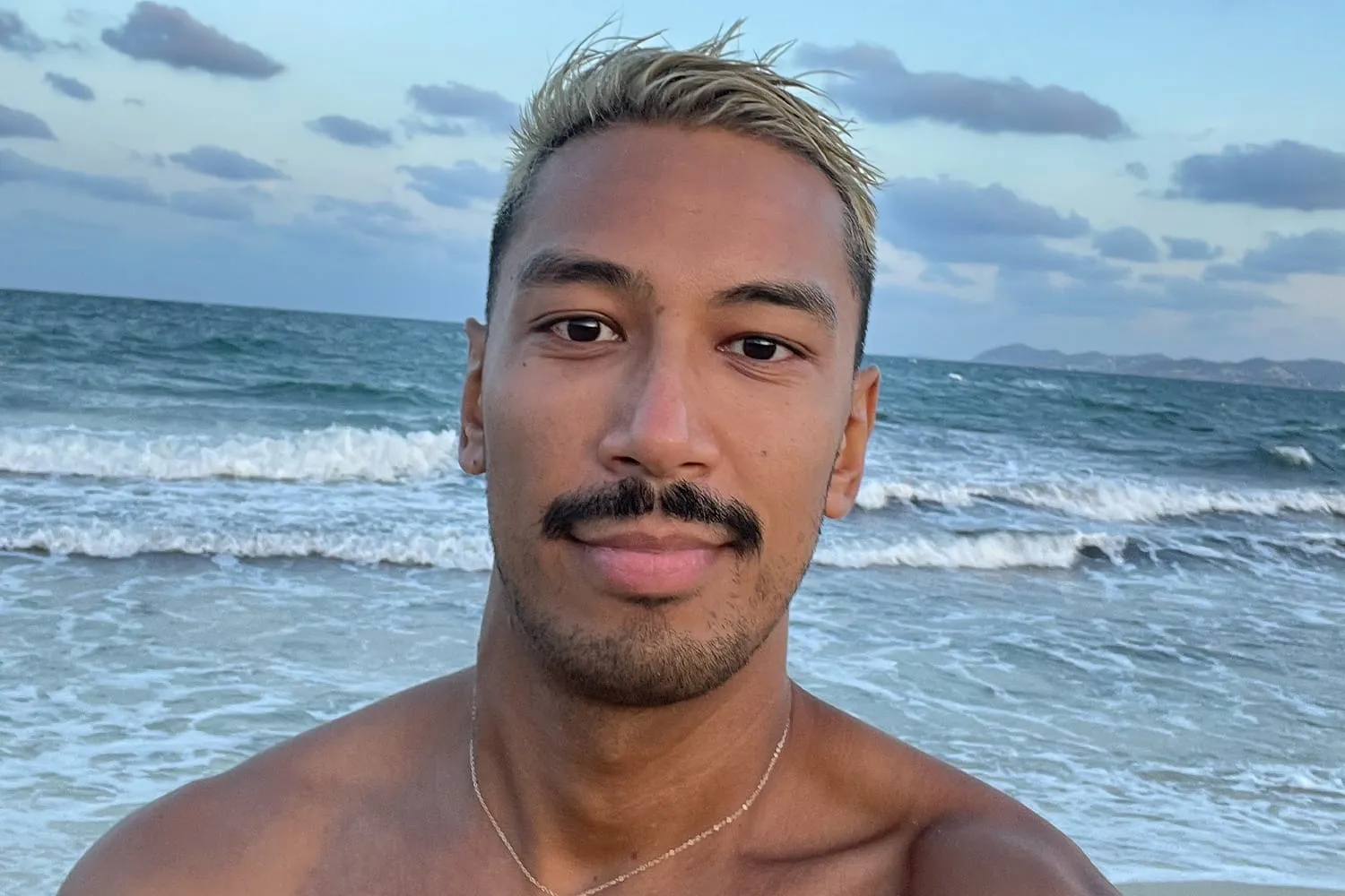 Shaun smiling at the beach with waves behind him