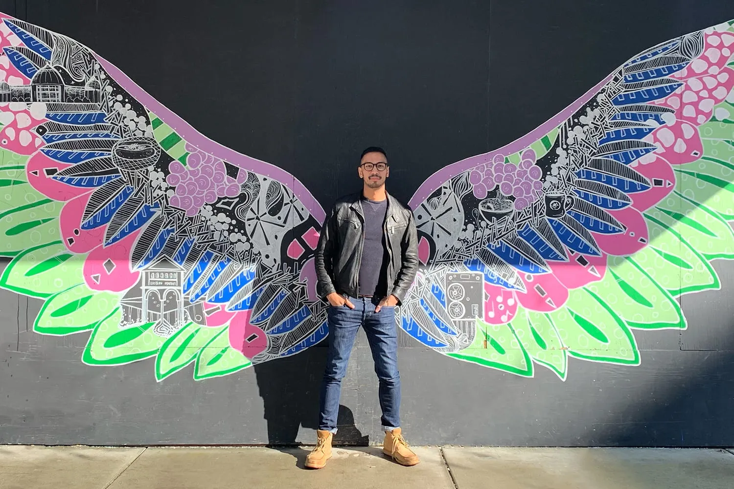 Shaun standing in front of a mural of painted wings