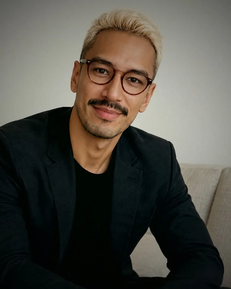 Shaun in a dark blazer, smiling on a couch